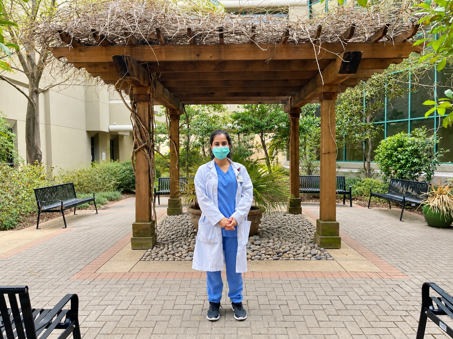 Dr. Remina Panjwani in scrubs, a white lab coat and a surgical mask, standing outside a hospital during the COVID-19 pandemic