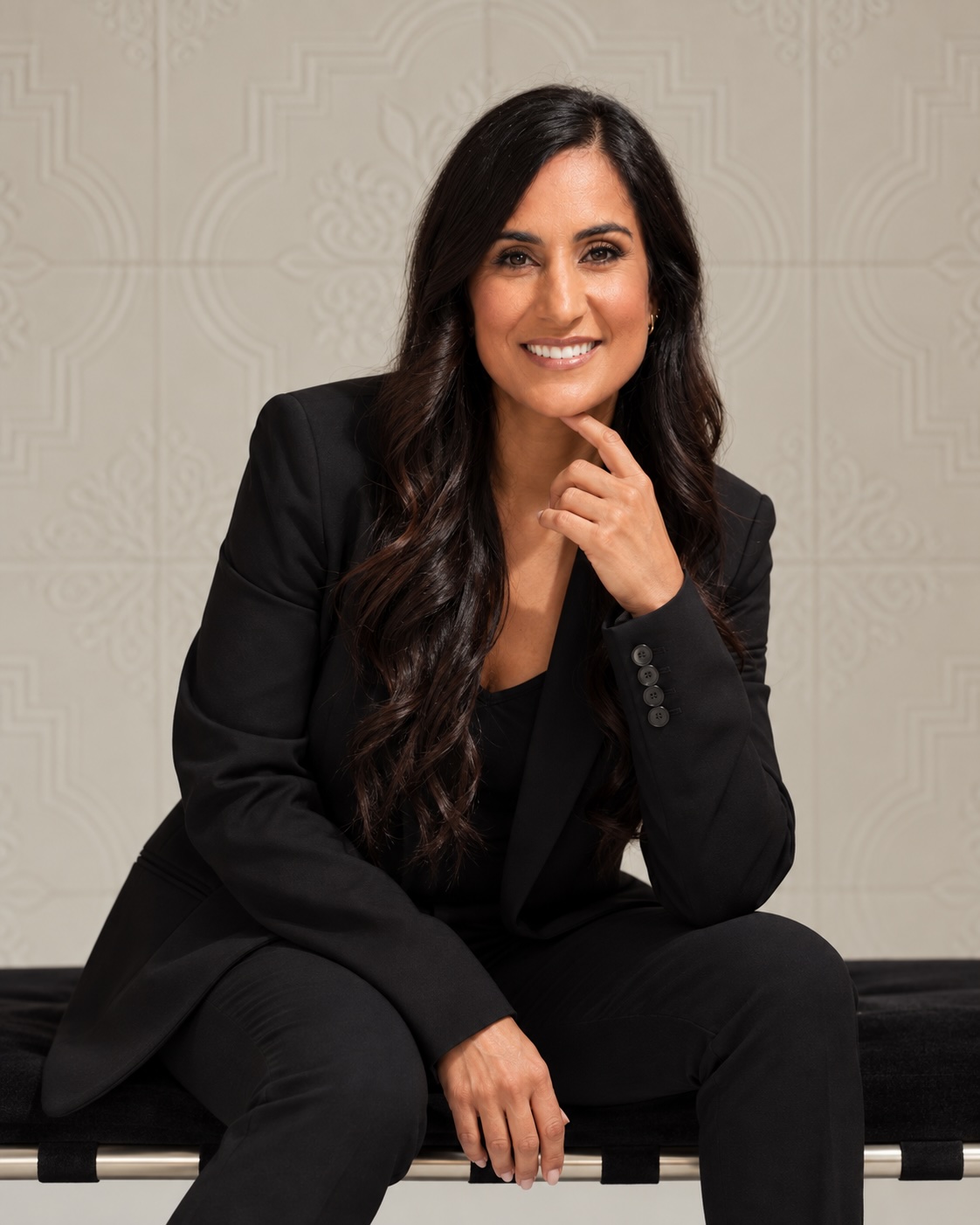 Dr. Remina Panjwani seated in a black suit, one hand resting below her chin