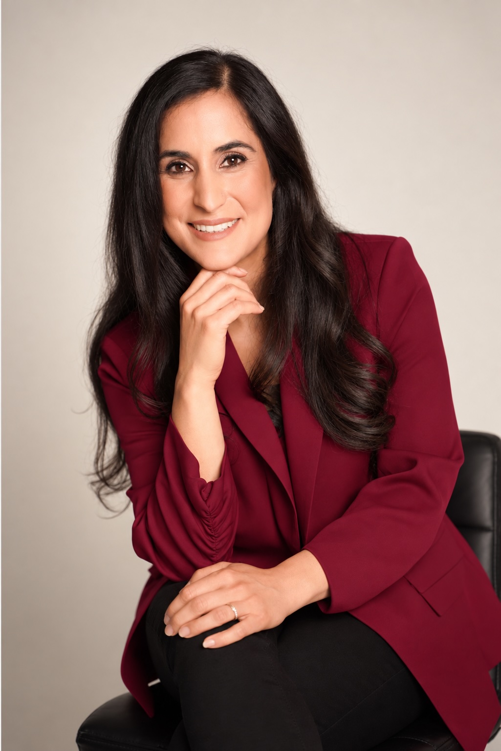Dr. Remina Panjwani in a deep red blazer, seated, resting her chin on her hand